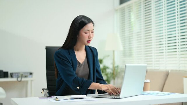 Asian businesswoman calculates financial data and taxes using a calculator and laptop at her modern office desk.