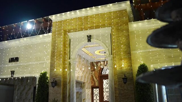 Beautiful nighttime view of a luxury wedding venue entrance decorated with glowing fairy lights, elegant architecture, chandeliers, and festive illumination. Perfect for wedding events, receptions, 