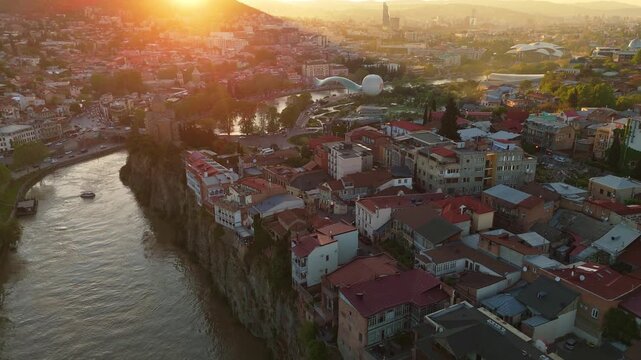 Warm golden hour aerial shot of historic houses perched on the Metekhi cliffs overlooking the Kura River in the ancient heart of Tbilisi, Georgia
