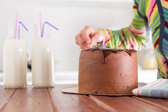 Side view of a Woman decorating a chocolate cake with buttercream icing and melted chocolate