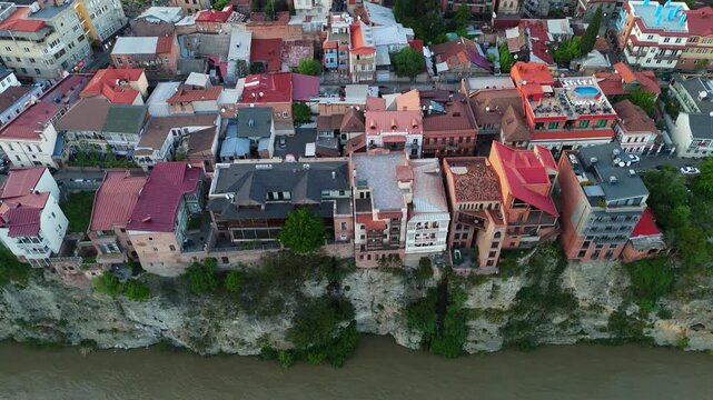 Top-down aerial view of colorful traditional houses perched on the steep Metekhi cliffs above the Kura River in the historic Old Town of Tbilisi, Georgia