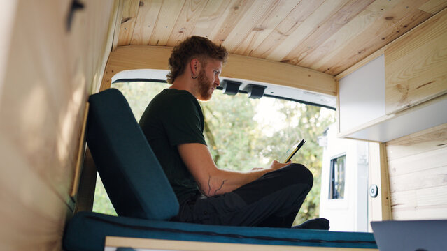 Man using tablet computer indoors in a wooden camper van, enjoying remote work and digital nomad lifestyle on the road