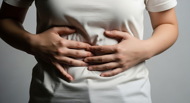 ​A person in a white t-shirt holding their stomach in pain to illustrate abdominal discomfort and digestive health issues.