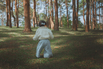Adorable little Asian girl in a fleece jacket exploring a scenic pine forest while holding a pine cone for outdoor adventure and childhood travel concept © oatawa