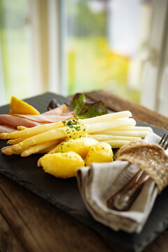 Seasonal white asparagus with creamy hollandaise sauce, served on a slate plate. Decoration suggestion for a modern seasonal cuisine. Vertical close-up.