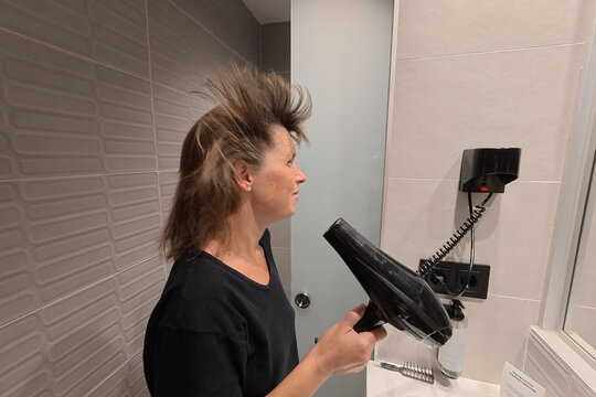 Young woman drying hair in bathroom creating a funny and voluminous hairstyle