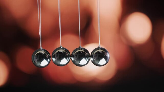 Newton cradle metal spheres swinging in slow motion against blurred golden background.