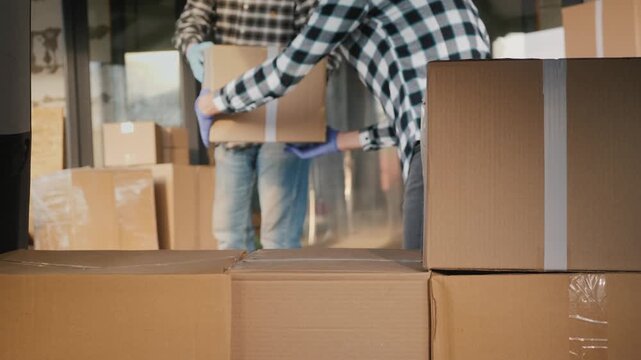 Two loaders in checkered shirts move cardboard boxes into a delivery van during the relocation process.