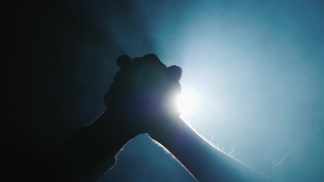 Silhouette of two people joining hands together against bright blue glowing light.