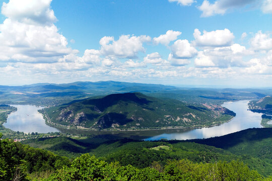 the riverbend of the Danube river at Zebegeny village and Nagymaros, Hungary. lush green hills in the background. popular summer holiday destination. smooth calm water surface. blue sky, white clouds