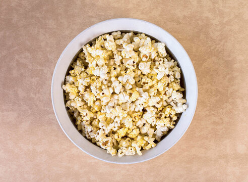 Fresh buttery popcorn served in white bowl on beige background