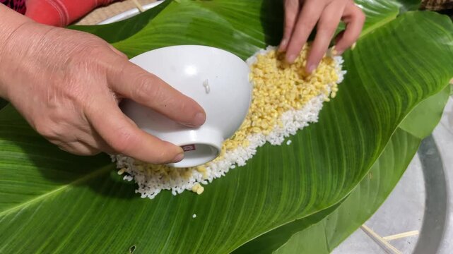 Woman&rsquo;s hands spreading sticky rice, mung beans, and pork on banana leaf to wrap banh tet in Vietnam for Tet food preparation and cultural cuisine themes.