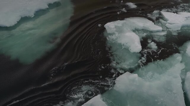 Aerial view of ice floes drifting in dark ocean water with gentle waves