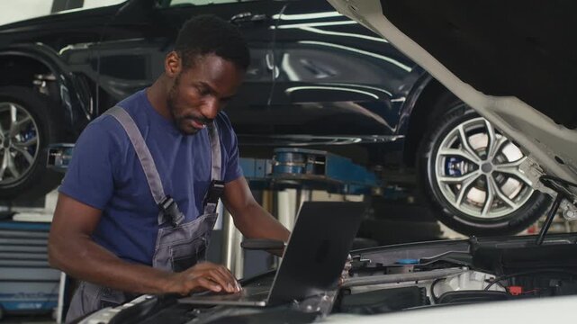 Car mechanic using a laptop to run diagnostic software for troubleshooting engine problems, modern computerised automotive repair.