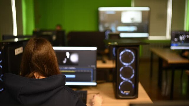Young woman student editing video content on computer with glowing rgb tower in modern media center.