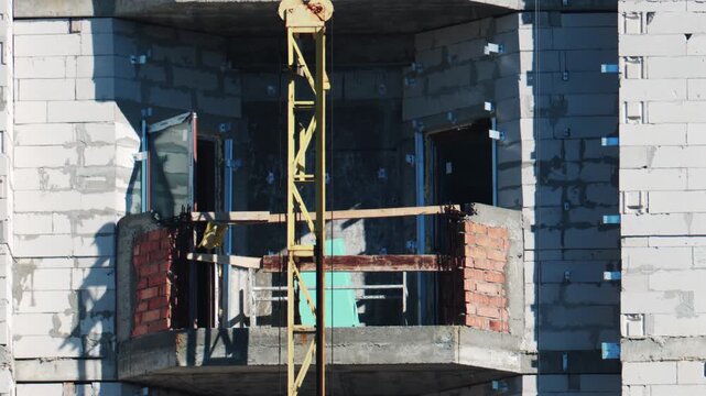 Construction site lift moving upward past balcony of residential building under development process.