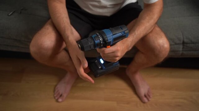 Young man assembling furniture with a cordless drill, doing home renovation and improvement work