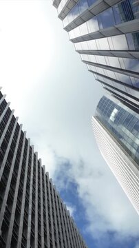 Low angle rotating view of modern skyscraper architecture with glass facades and corporate offices reflecting the blue sky and clouds in a financial district center