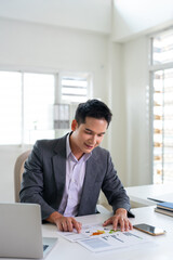 Fototapeta premium Confident young businessman auditing revenue report and planning budget while working at desk in office.