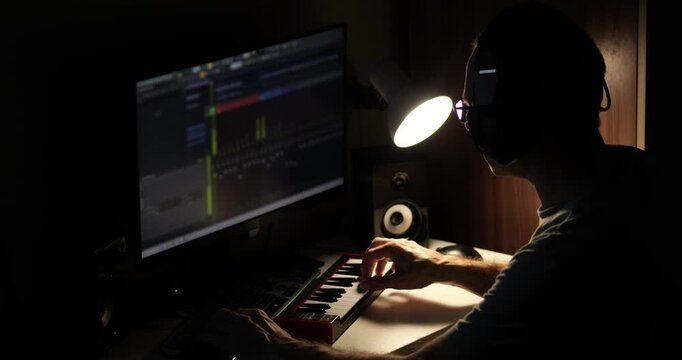 Creative content creator producing music in home studio using keyboard and computer software. Digital workflow of modern musician, concept of online creativity, remote work and content production