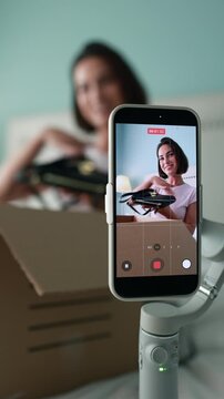 Middle-aged woman blogger recording an unboxing video using smartphone camera. Person capturing content for social media, apps. Lifestyle Technology. Engages audience. Vertical footage