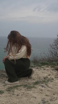 Woman dancing cliffside young female with long hair performs expressive dance moves on a scenic coastal overlook with sea view
