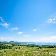 Fototapeta premium Scenic coastal landscape with rolling green hills and distant ocean under blue sky