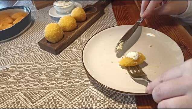 Crispy cheese balls served on plate on wooden table in cozy restaurant setting. Close-up of female hands using cutlery during lunch.