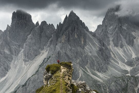 Man with red jacket standing on one degree, behind him mountain peaks and pointed rocks, dramatic clouds, Cimon the Croda Liscia and Cadini group, Auronzo di Cadore, Belluno, Italy