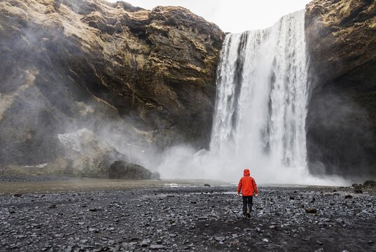 Hiker with red jacket in front of a high waterfall Skogafoss, Skogar, South Iceland, Iceland