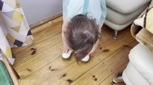 little girl sitting on a pouf and playing with her shoes