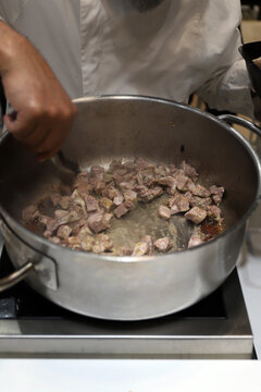 chef guisando carne en una olla en los fogones de la cocina