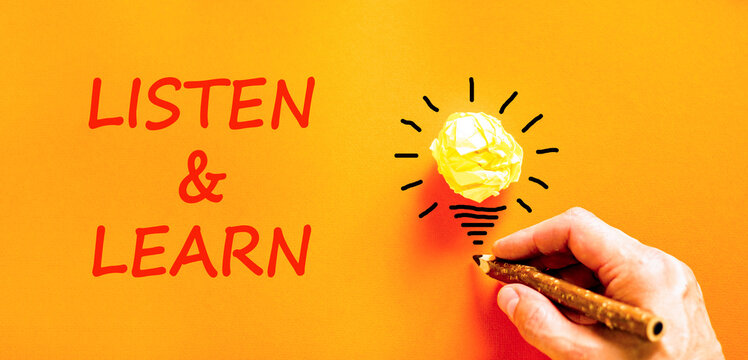 Listen and learn symbol. Concept words Listen and learn on beautiful orange paper. Beautiful orange background. Light bulb icon. Businessman hand. Business listen and learn support concept. Copy space