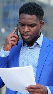 Focused Contract Review. Urban Office Worker Carefully Examining Contractual Details. Urban Professional In Blue Suit Scrutinizing Contract Terms During Telephone Call With Focused Intensity