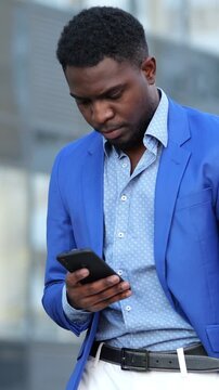 Urban Businessman In Blue Suit Checks Urgent Communication Tense Expression. Concerned Executive Dressed In Blue Examines Urgent Message Near Modern Glass Building With Worried Demeanor