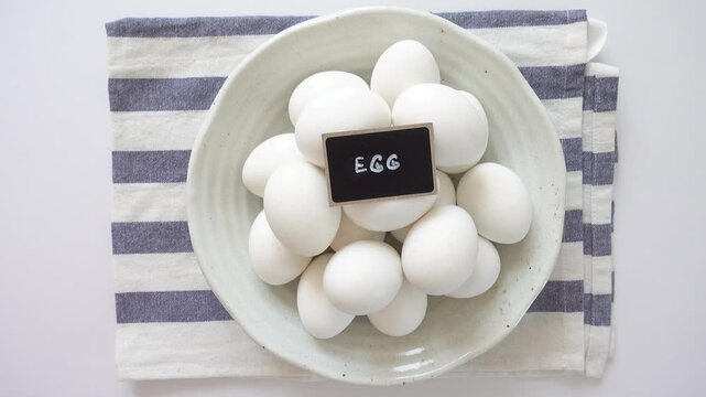 Woman's hand and a ceramic bowl with white eggs on a striped kitchen napkin. Healthy eating, keto and paleo diet concept. High-protein foods. Ideal for nutrition, cooking and dietary lifestyle content