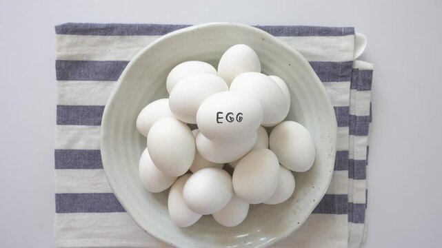Woman's hand and a ceramic bowl with white eggs on a striped kitchen napkin. Healthy eating, keto and paleo diet concept. High-protein foods. Ideal for nutrition, cooking and dietary lifestyle content