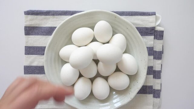 Woman's hand and a ceramic bowl with white eggs on a striped kitchen napkin. Healthy eating, keto and paleo diet concept. High-protein foods. Ideal for nutrition, cooking and dietary lifestyle content