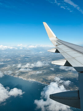 Airplane wing view above clouds and coastline under a blue sky, aerial travel scene showing flight, landscape and summer vacation journey
