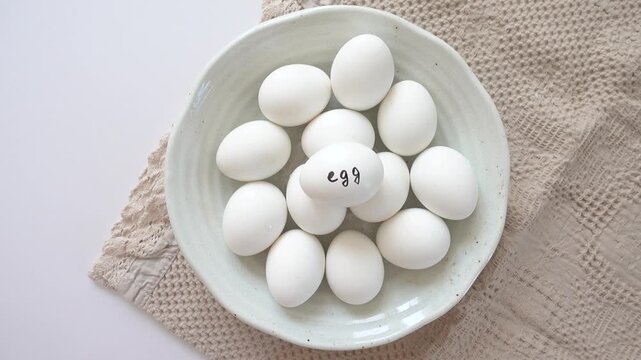 Woman's hand and a ceramic bowl with white eggs on a striped kitchen napkin. Healthy eating, keto and paleo diet concept. High-protein foods. Ideal for nutrition, cooking and dietary lifestyle content