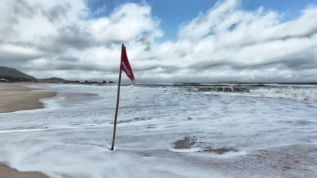 Rote Warnflagge mit Aufschrift &bdquo;LOCAL PERIGOSO&ldquo; an einem Sandstrand in Brasilien bei starkem Wellengang