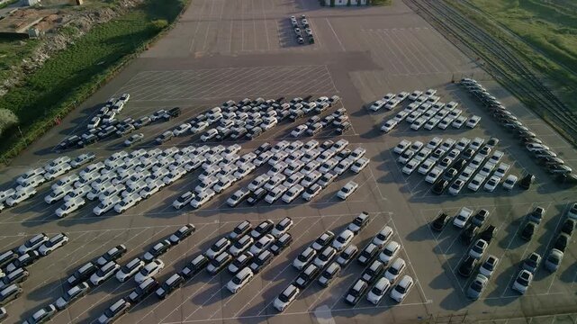 Cinematic drone flight over rows of new cars at a massive parking lot. Automotive industry logistics and vehicle distribution hub.