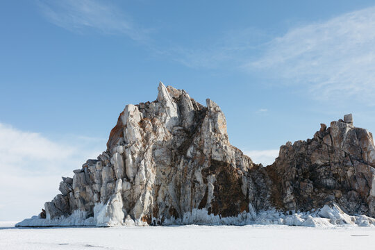 Winter landscape with Shamanka Rock rising above the frozen surface of Lake Baikal near Khuzhir, Olkhon Island, Irkutsk Oblast, Russia under blue sky