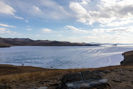 Wide winter landscape of Ogoy Island and the frozen surface of Lake Baikal with ice patterns, hills and clouds, natural travel scenery in Irkutsk Oblast, Russia