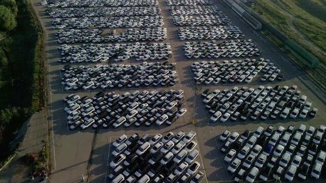 Cinematic drone flight over rows of new cars at a massive parking lot. Automotive industry logistics and vehicle distribution hub.