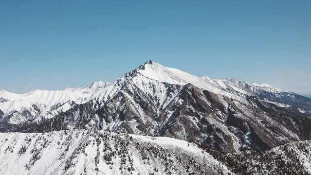 Panoramic view of the snow-covered Peak of Love above Arshan village in Buryatia, Russia, with rugged ridges and clear blue sky on a sunny winter day