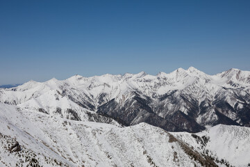 Obraz premium Wide panoramic view of snow covered mountain ridges and valleys under clear blue sky, photographed from Peak Galina near Arshan, Buryatia, Russia in winter daylight