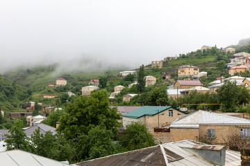 Obraz premium Panoramic view of Kubachi village on a green mountain slope with stone houses and metal roofs, low clouds and fog after rain, Dagestan, Russia, Caucasus