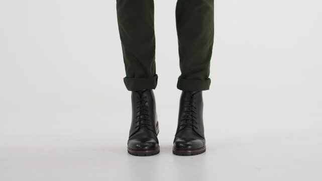 Person in green pants and black leather combat boots tapping foot on an isolated white background, showcasing stylish footwear