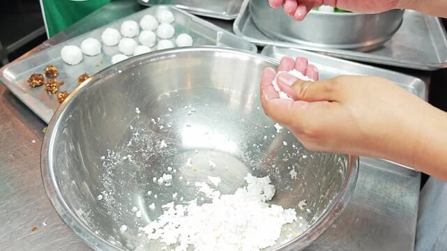 Hands molding sago balls with sweet pork stuffing in a kitchen.